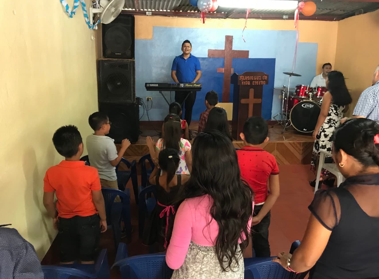 Niños y adultos en una iglesia pequeña frente a un hombre tocando el teclado.